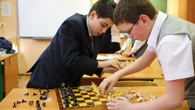 Two boys put the chess pieces, teacher and other two children in the background