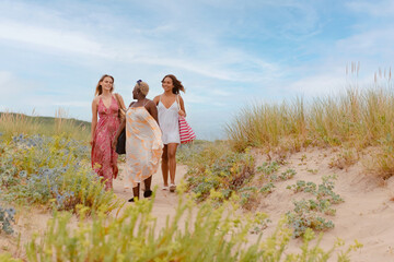 multiracial group of three young girls walking together on the beach during a summer trip.