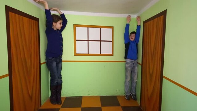 Happy boy and girl pose in room with optical illusion