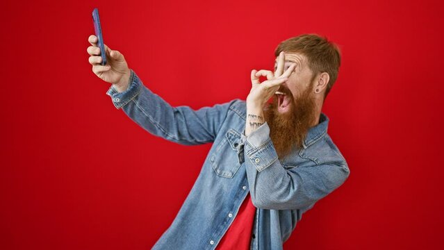 Confident young redhead guy, happily making a cool selfie with his phone over an isolated red background. smiling, he radiates positive vibes and joy.