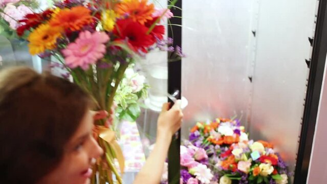 Girl with bouquet of gerberas opening door to cold room with flowers