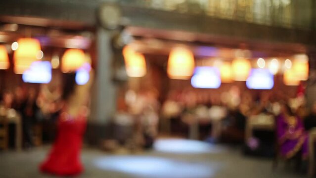 Woman in red dress dancing in hall of restaurant is blurred.