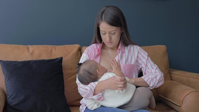 Mom cleaning her baby with a wet towel while feeding him in the living room of her house. Breastfeeding at home