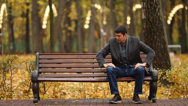 A young man sits on the edge of the bench and sits down in the middle
