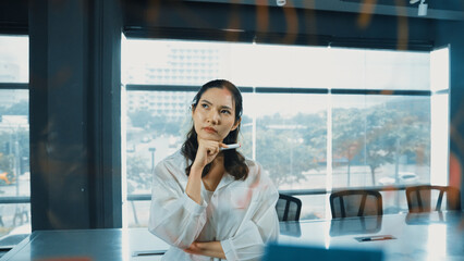 Beautiful female leader thinking about start up project in front of glass board. Smiling young...