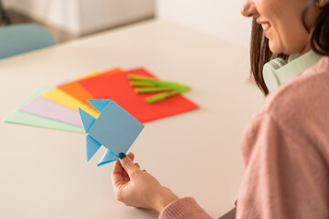 Delighted woman holds up a blue origami fish, possibly crafting a playful April Fools' Day gag.