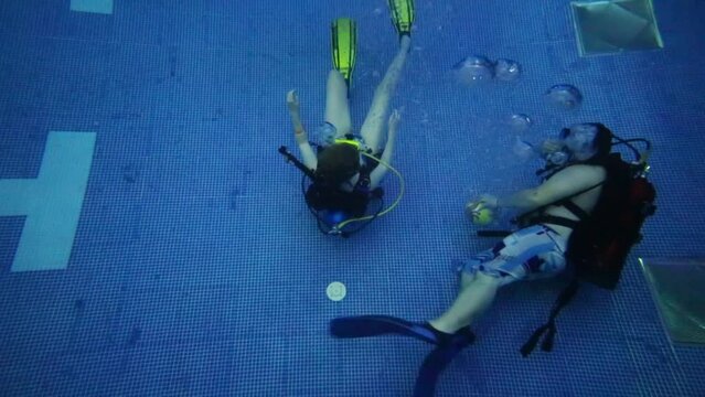 Three divers with scubas swim underwater close to bottom of pool