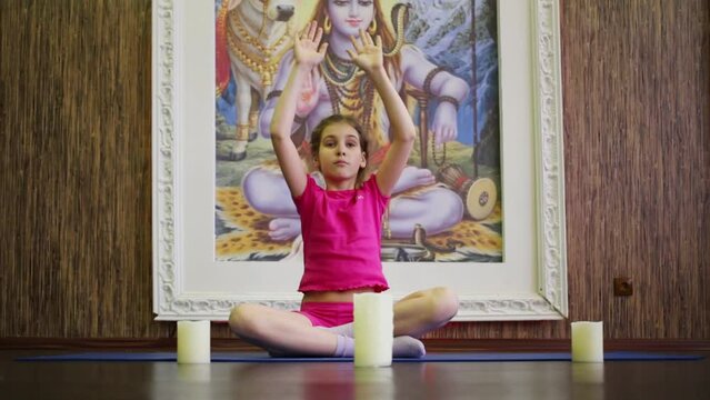 Girl sits on floor in pose of lotus near three candles