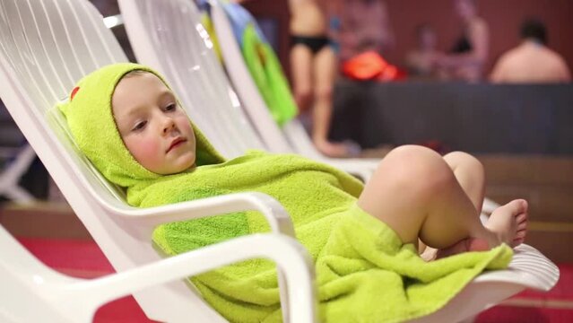 Boy wrapped in a towel resting on a lounger in the aquapark