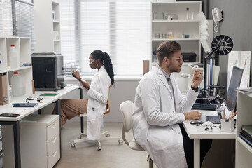 Side view of Caucasian male technician holding 3D dental model and looking at computer screen while...