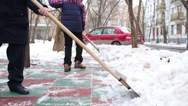 Two boys clean artificial covering of playground with snow shovels.