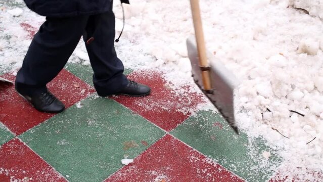 Two boys clean artificial green-red covering with snow shovels.