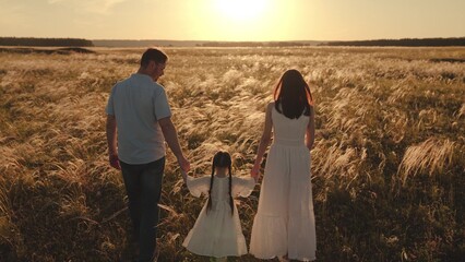 Family walking through field of wheat with setting sun on background. Family savores time with...