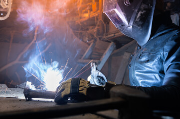 welder in a workshop welds a metal part. General plan of an old cluttered garage where a man in...