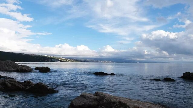 Real time wavy sea surface in a bay with beautiful rocks. Magnificent meditative nature landscape with Rijeka in the background. White clouds above the blue water on a sunny winter afternoon.