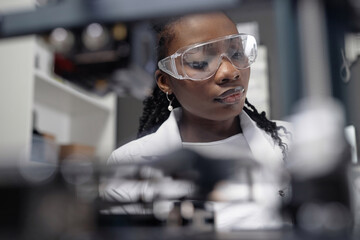 Look through blurred 3D printer components of young Black woman laboratory specialist in protective...