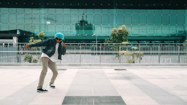 Happy hipster listen to hip hop music from headphone while dancing in lively mood. Professional street dancer perform b boy dancing at outdoor. Outdoor sport 2024. Modern lifestyle. Sprightly.