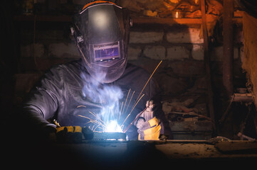 Village workshop, welding in an old garage. An unrecognizable man repairs a metal part wearing protective gloves and a mask
