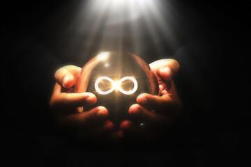 Infinity Symbol Glowing in Crystal Ball : Mysterious hands cradle a crystal ball emitting a bright...