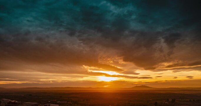 Time-lapse of a sunset over a volcano with cloudy sky, hills in the background, and mist.