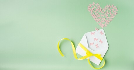 Paper craft for Valentine's Day. On a green background there is an applique of colored paper butterflies in the shape of a heart flying out of an envelope. Handmade concept, Valentine's Day holiday.