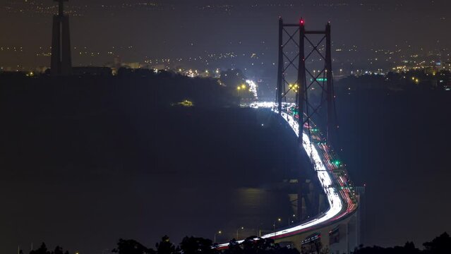 Panoramic view over Lisbon and Almada with traffic on illuminated April 25 bridge from a viewpoint in Monsanto night timelapse. Aerial top overview with Cristo Rei monument
