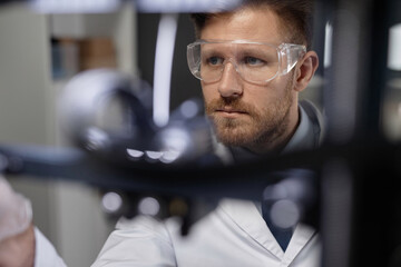 Medium close up shot of focused Caucasian male technician in protective goggles working in...
