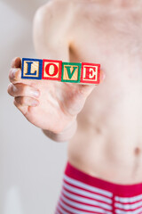 A man in underwear holding blocks in his hand that spell out the word LOVE