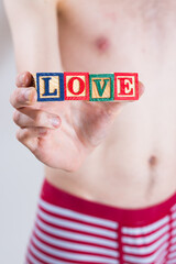 A man in underwear holding blocks in his hand that spell out the word LOVE
