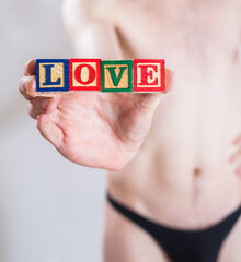 A man in underwear holding blocks in his hand that spell out the word LOVE