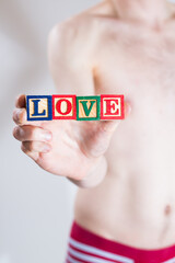 A man in underwear holding blocks in his hand that spell out the word LOVE