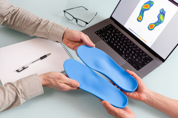 Female doctor orthopedist  presents new custom made insoles to a male patient in a clinic. - 718339897