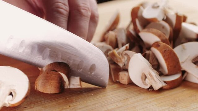 Chef cutting the mushrooms on a wooden board with knife, mushroom cooking close up. 