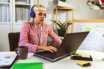 Young blonde woman smiling while working on her laptop and drinking coffee