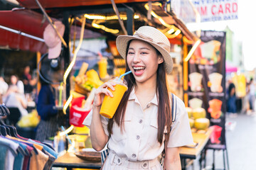 Young Asian woman traveler tourist buying a freshly made juice and walking at outdoor market in...
