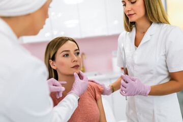 A doctor examines the patient before the aesthetic procedures. The patient looks at herself and tells her what she wants to change.