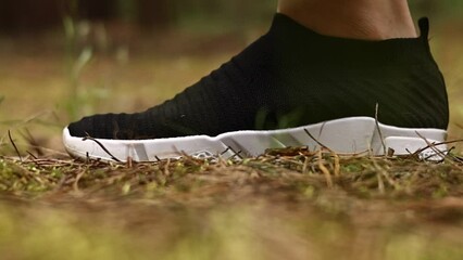 Cropped shot of female or male feets in black sneakers with white sole step on grass in spring or autumn at the park. Legs walking, side view. Close up running shoes. Leisure activity concept.
