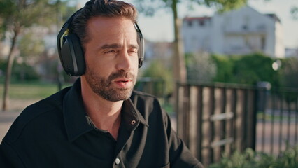 Headphones guy listening music sitting sunlight city park close up. Man headset