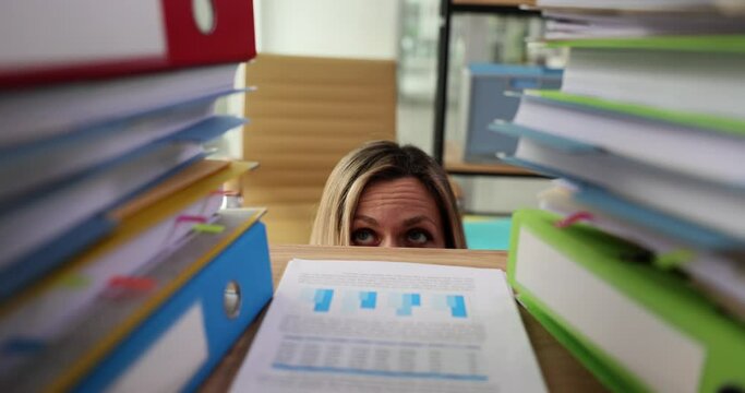 Business woman hiding behind desk and afraid of paperwork