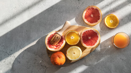 Fresh citrus fruits on wooden board, wooden juicer and a glass with juice. Natural light. Vibrant, juicy and delicious scene, top view.