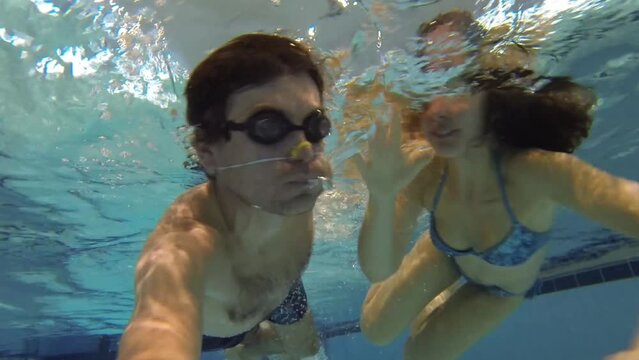 Man in goggles swims with woman in indoor pool and makes selfie
