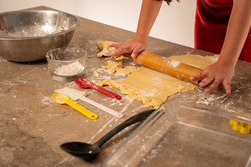 manos de niña preparando y amasando con rodillo la masa para hacer galletas con varios utensilios...