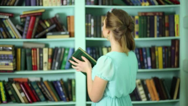 Beautiful young woman puts book on shelve in library