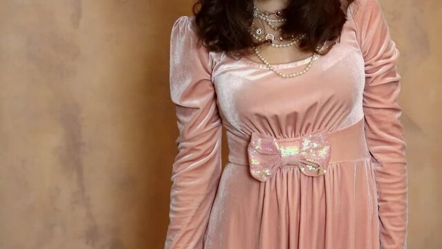 Woman with necklace touches her skirt near wall in studio