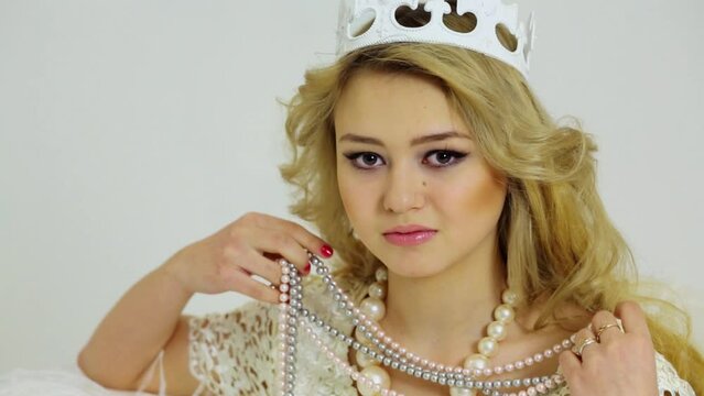 Young blonde with crown on curly hair hold pearl beads
