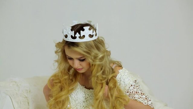 Young blonde in crown holds beads of huge artificial pearls