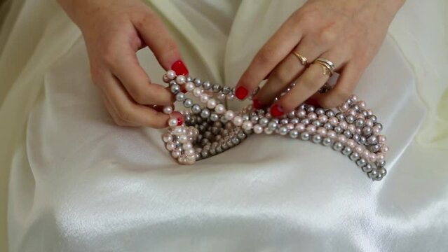 Woman hands hold artificial pearl beads on white dress