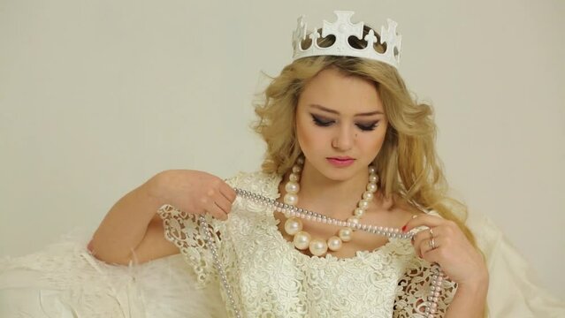 Young brunette tries on some beads with necklace and crown on head