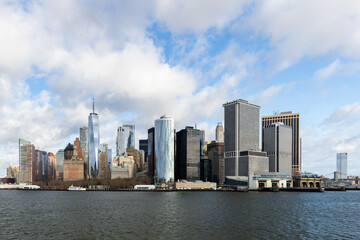 A skyline view of Lower Manhattan of New York from the bay with blue sky and clouds.