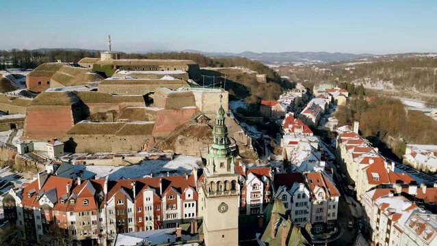 Historical clock tower of Klodzko town hall with fortress in the background. Old town city hall close up. Winter cityscape panorama, aerial view.